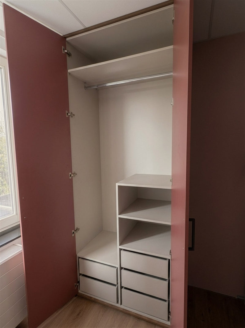 Zijn kast van binnen: links een hoog hanggedeelte voor haar lange kleding, rechts open vakken en lades, in een lichte binnenkast in muisgrijs.